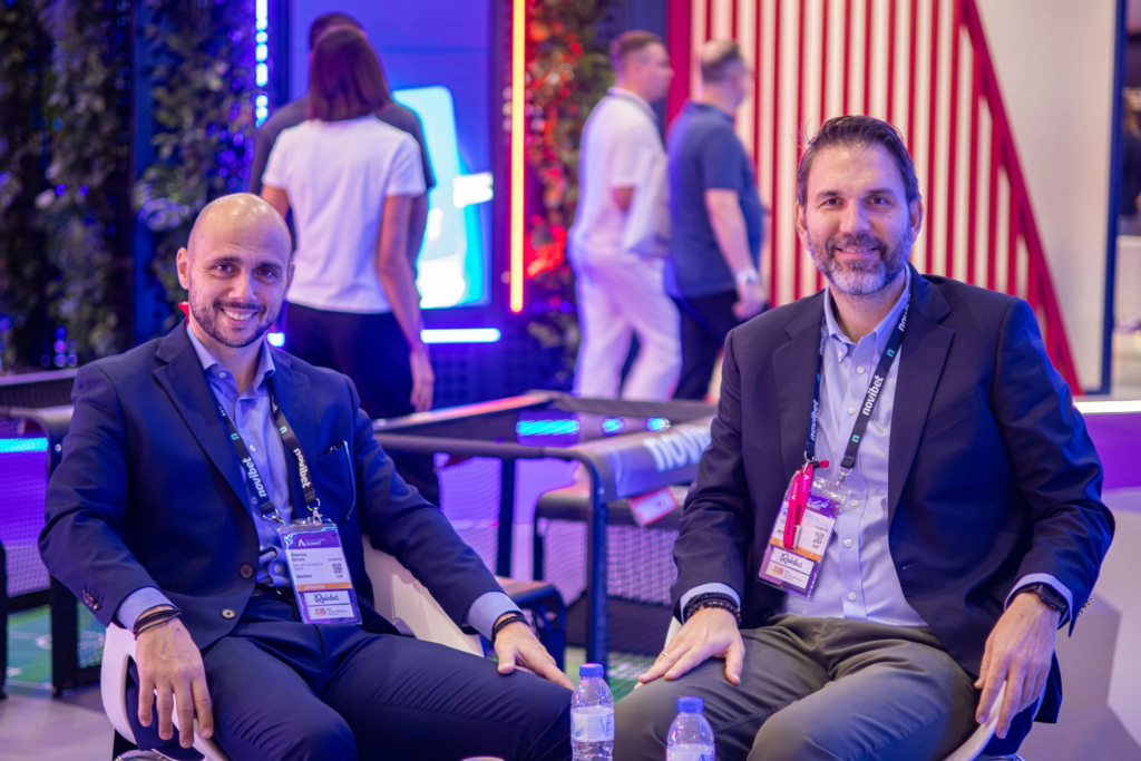 Corporate team networking at SBC Lisbon conference booth. Team members in branded shirts at professional event, FIL congress center.